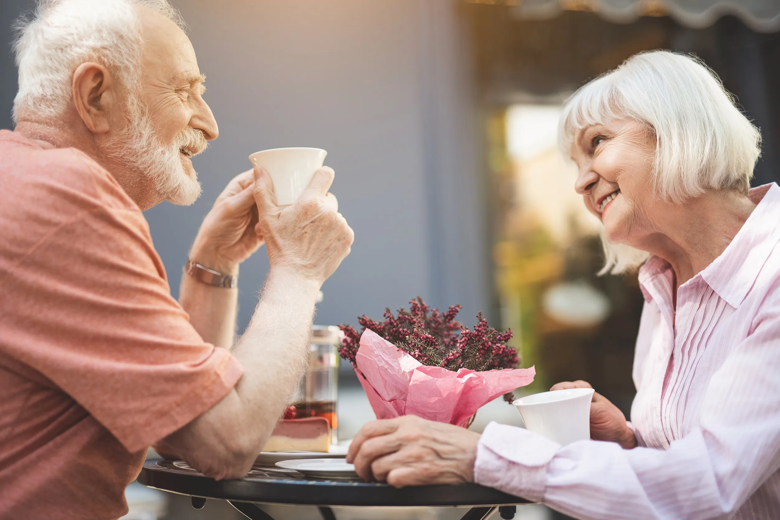 Side view profile of happy senior couple drinking tea in cafe outdoors